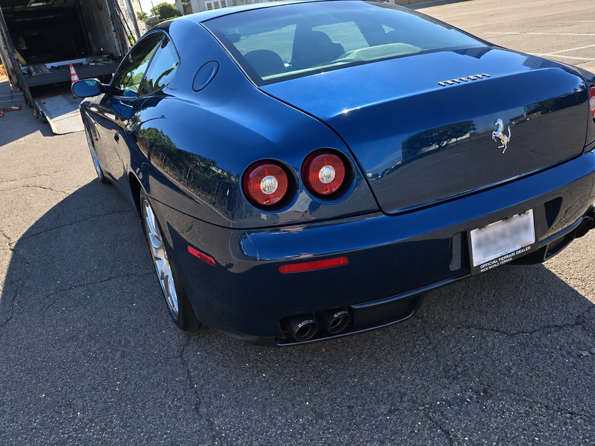 Rear view of the blue 2005 Ferrari 612 Scaglietti beside an enclosed auto hauler in Stamford, Connecticut